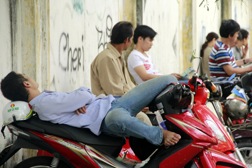 Tại địa điểm thi THPT Trưng Vương (quận 1, TP HCM) một người đàn ông tranh thủ nằm ngủ trên xe máy.