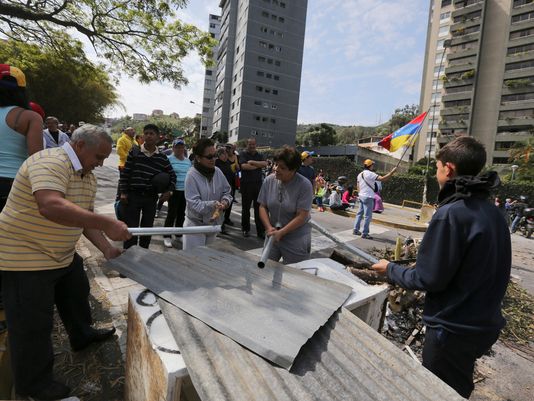 Người biểu tình gõ vào một tấm tôn trên đường phố Caracas hôm 20-2. Ảnh: AP