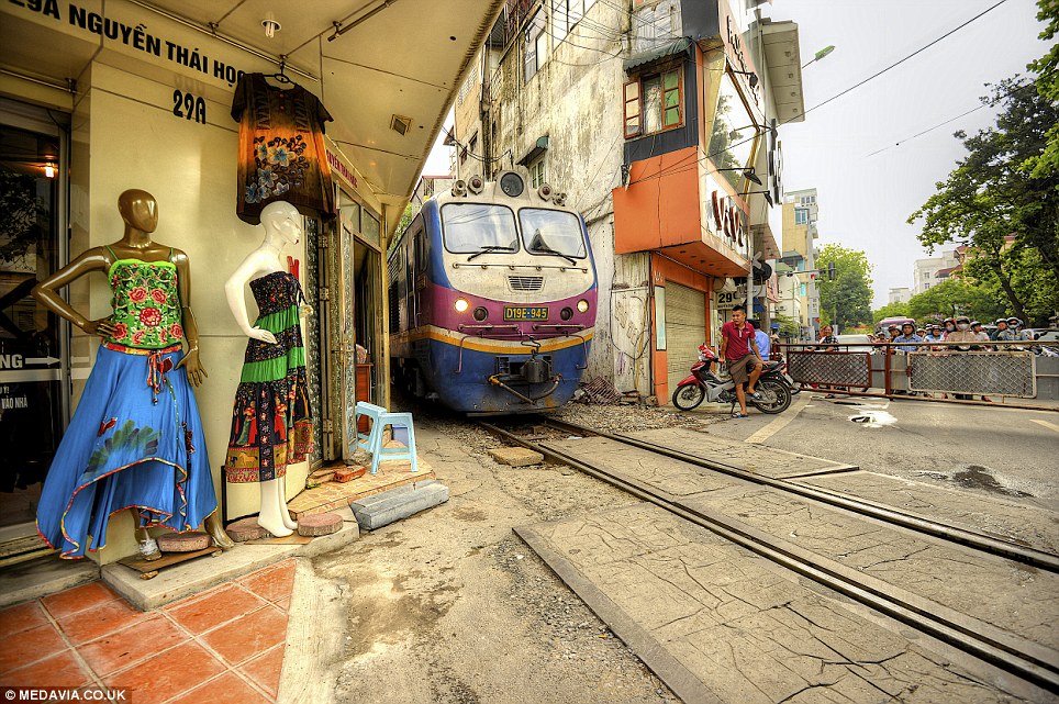 Tight space: A train squeezes past a shop display in the centre of Hanoi, Vietnam, while a man on a moped waits for the tracks to clear