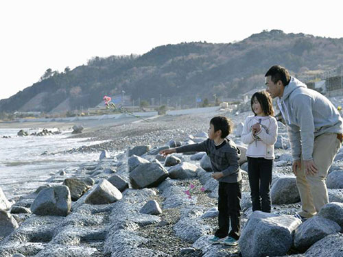 Ba cha con anh Atsushi Niizuma mang hoa hồng đến bên bờ biển tỉnh Fukushima Ảnh: KYODO