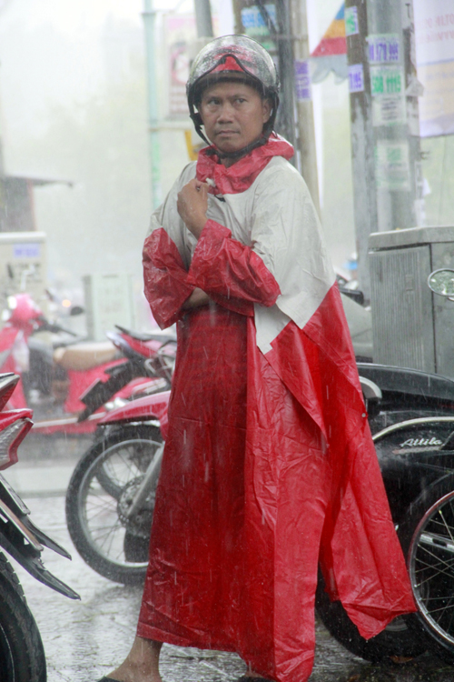 Chú Tâm (quê Bình Thuận) mặc áo mưa, đội mũ bảo hiểm đứng chờ con thi trước cổng trường giữa cơn mưa lớn. (Ảnh chụp sáng 9 – 7).