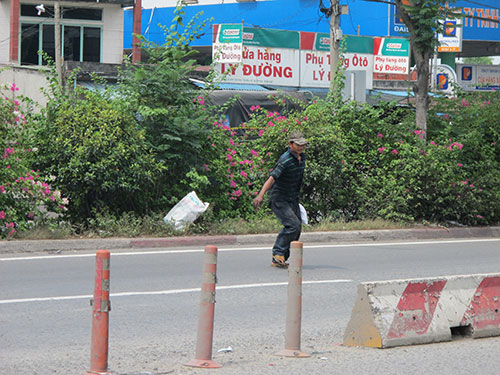 Một người đi bộ băng qua tim đường bằng cách kéo dây thép, cây bông giấy trên tuyến Quốc lộ 1 trước chợ đầu mối Thủ Đức, TP HCM