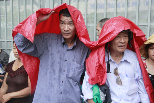 Hai người đàn ông này cùng che chung môt chiếc áo mưa trước hội đồng thi Trường Nguyễn Thị Minh Khai (quận 3)