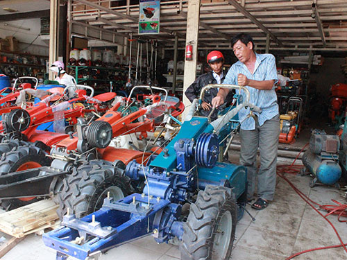 Nguyễn Văn Hai (phải) hướng dẫn khách hàng cách sử dụng sản phẩm cơ khí do anh tự chế