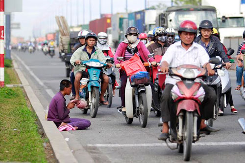 Một người xin ăn bên vệ đường đầy xe cộ trên xa lộ Hà Nội Ảnh: HOÀNG TRIỀU