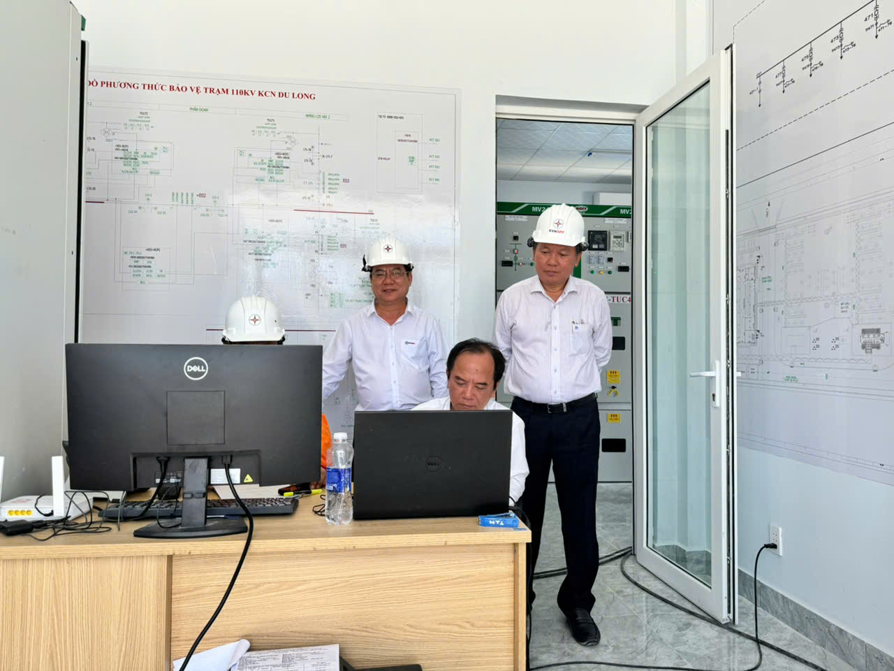 A group of men in hardhats standing in front of a computer  Description automatically generated