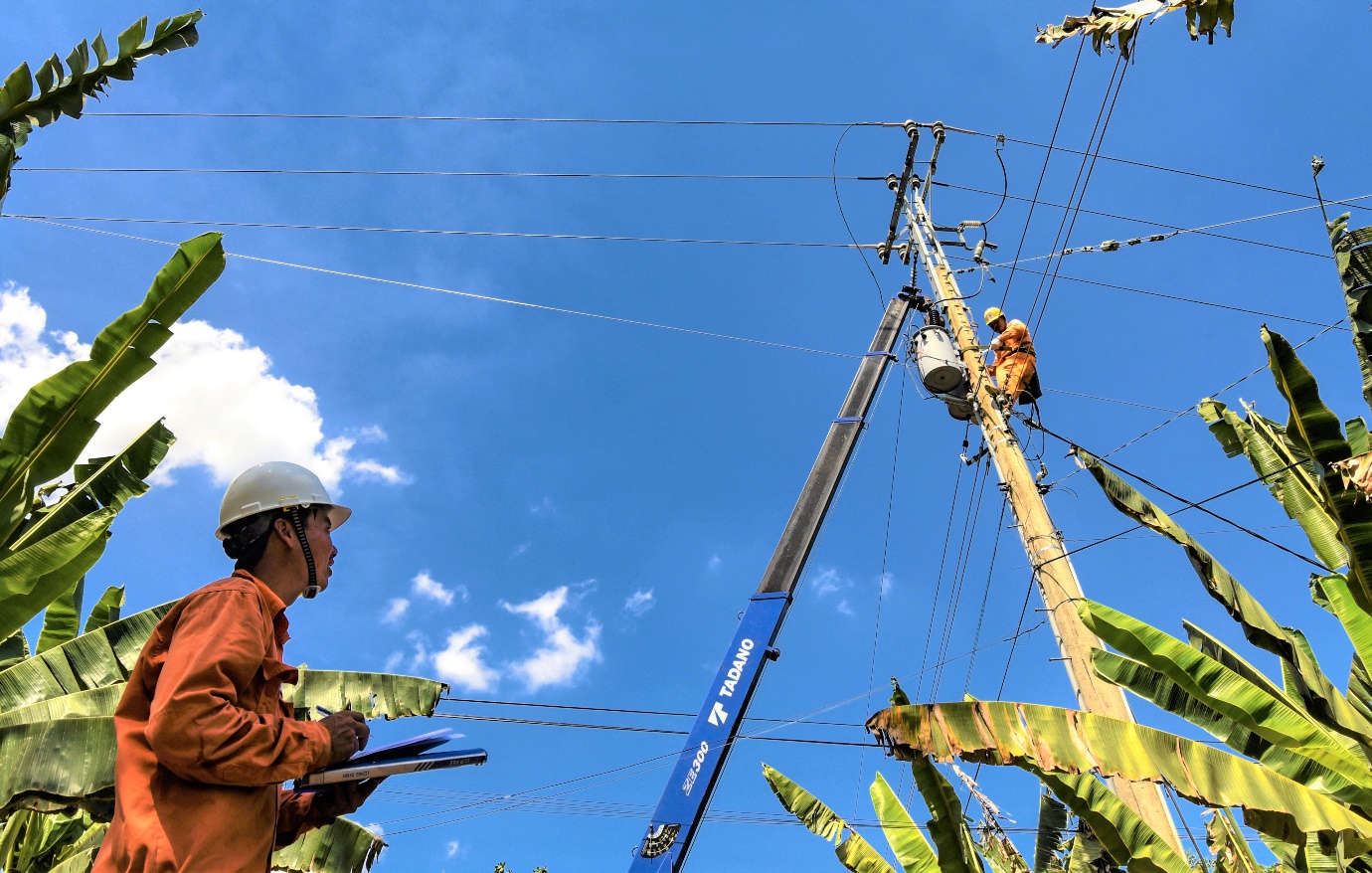 A person in a white helmet and orange jumpsuit working on a power line  Description automatically generated