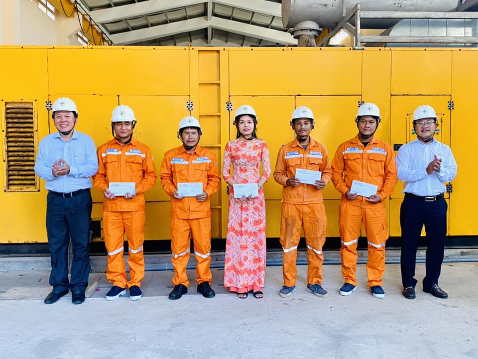 A group of people in orange jumpsuits and helmets standing in front of a yellow wall  Description automatically generated