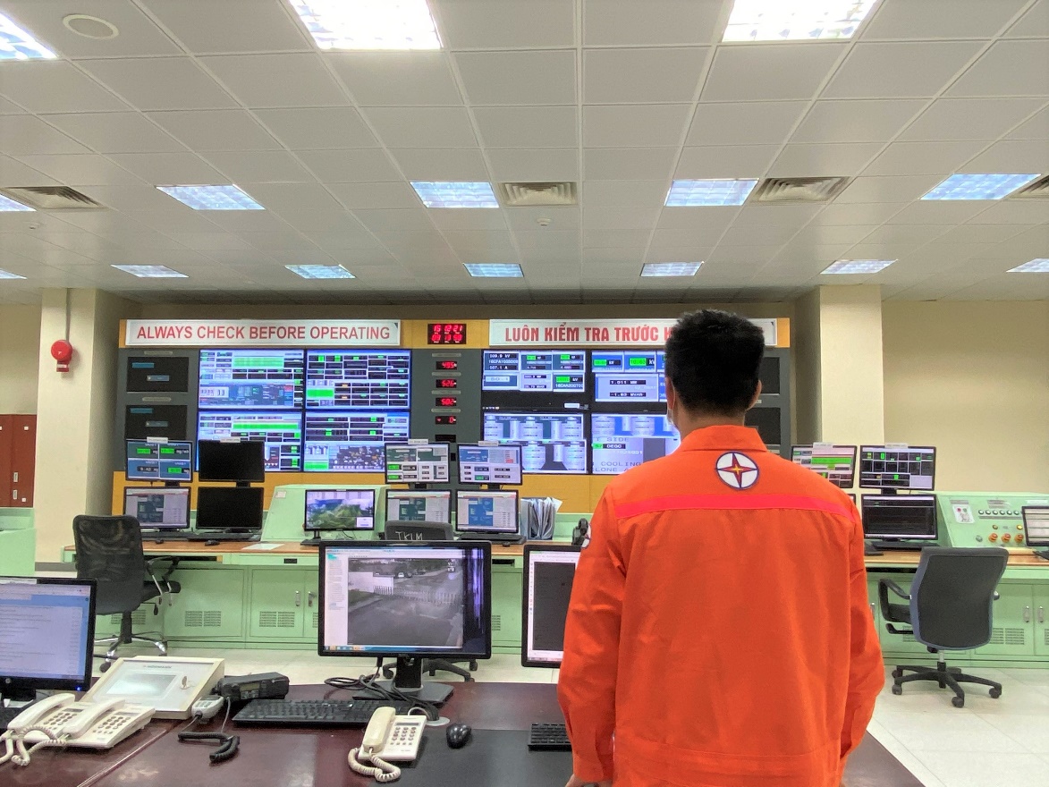 A person in an orange jumpsuit looking at a large screen  Description automatically generated