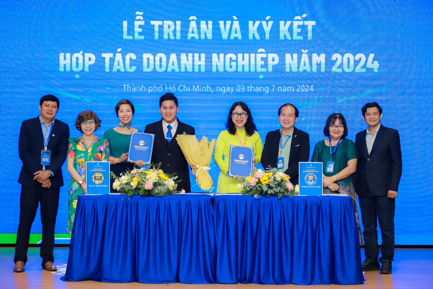 A group of people standing at a table with blue signs  Description automatically generated