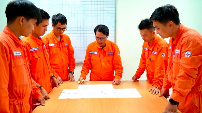 A group of people in orange jumpsuits looking at a piece of paper  Description automatically generated