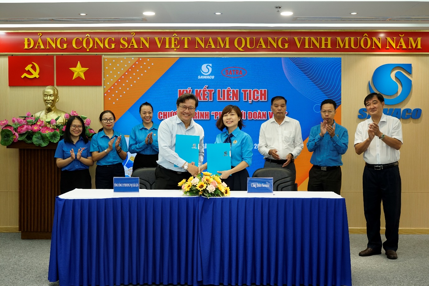 A group of people standing at a table with blue cloth  Description automatically generated