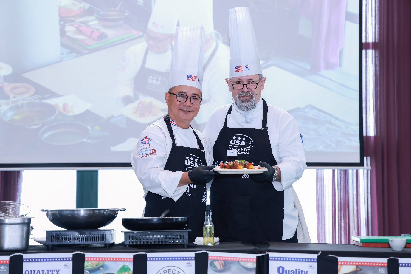 Two men wearing chef's hats and aprons holding a plate of food  Description automatically generated