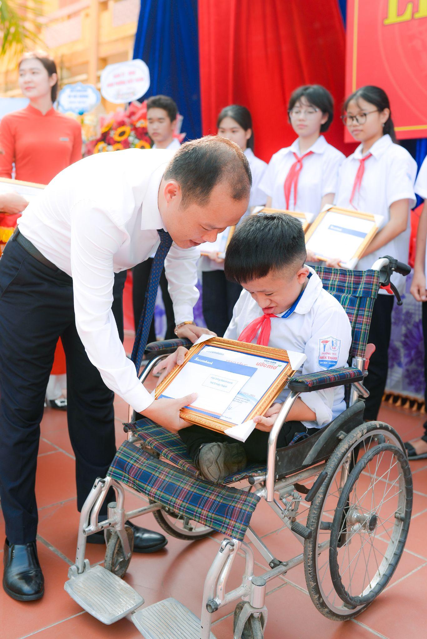 A person showing a child a certificate to a child in a wheelchair  Description automatically generated