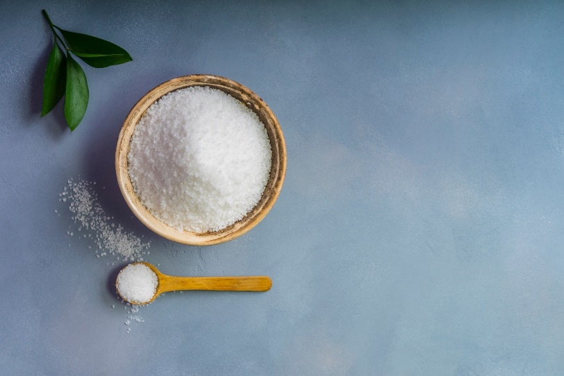 A bowl of salt next to a spoon and a plant  Description automatically generated