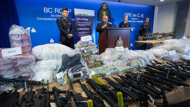 A table laden with piles of drugs and lines of guns at a news conference