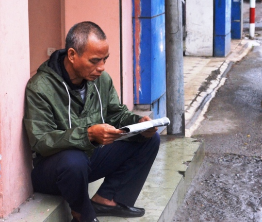 Mưa rét không có khách, một bác lái xe ôm trên đường Tôn Đức Thắng ngồi tranh thủ đọc báo