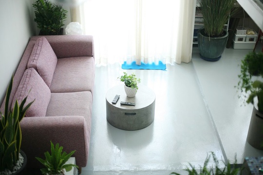 Để hạn chế cảm giác lạnh lẽo của màu tường và sàn, đồ đạc được chọn làm điểm nhấn màu sắc, như ghế ở chỗ làm việc có màu đỏ, sofa hồng tím. Góc sofa cùng chiếc bàn trà đúc bằng xi măng là nơi yêu thích nhất của chủ nhà. Mỗi khi ngồi xem tivi, trước mắt chủ nhà sẽ là một khu vườn xanh mướt dễ chịu.