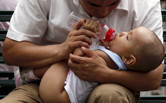 Một người đàn ông đang cho con bú ở trung tâm TP Bắc Kinh. Ảnh: Reuters