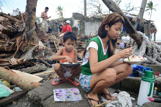 Người dân Philippines ăn uống bên ngoài những căn nhà đổ nát ở tỉnh Sorsogon,miền trung Philippines hôm 15-12. Ảnh: REUTERS