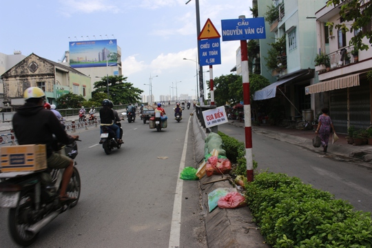 
Ngay chân cầu Nguyễn Văn Cừ là bãi rác lớn, bên trên đặt một biển rao bán cua biển của gánh hàng rong trên cầu.

