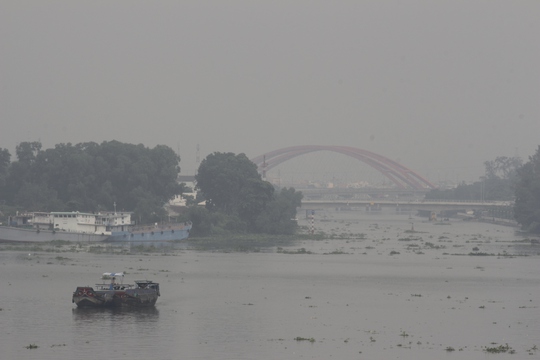 Trên sông Sài Gòn, thuyền bè phải di chuyển chậm để tránh đâm vào nhau do tầm nhìn hạn chế. Đằng xa, cầu Bình Lợi mờ ảo trong mù khô che phủ.
