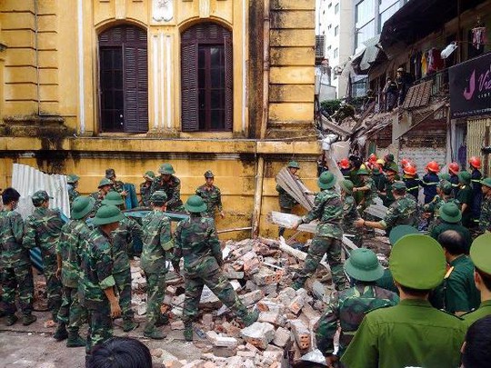 Lực lượng cứu hộ tiếp tục dùng tay và dụng cụ để đưa gạch ngói, tấm tôn, đồ đạc đổ nát ra ngoài sau khi máy xúc hoạt động xong