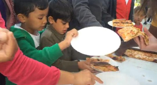 Những người nhập cư nhận bánh pizza. Ảnh: NBC News
