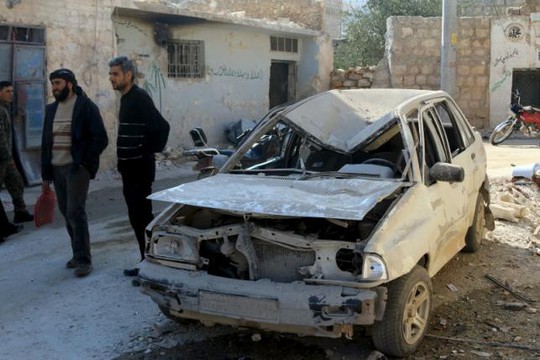 Hai người đàn ông đứng cạnh một chiếc xe hơi bị phá hủy tại Darat Izza, tỉnh Aleppo ngày 28-2. Ảnh: Reuters
