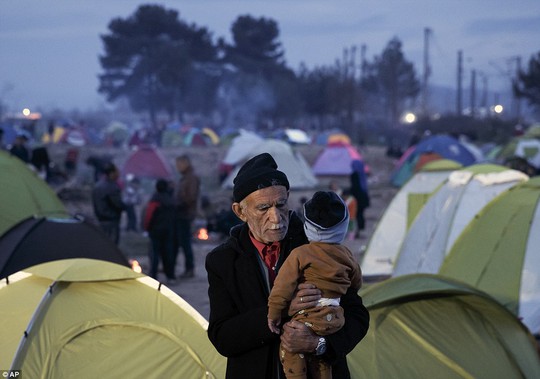 
Cụ ông bế đứa cháu nhỏ tại Idomeni giữa bộn bề những chiếc lều tị nạn sau lưng. Ảnh: AP
