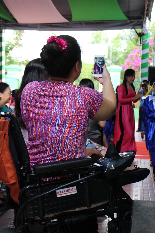 Một phụ huynh ngồi trên xe lăn ghi lại khoảnh khắc ra trường của con ở Trường Mầm Non Nam Sài Gòn Ảnh: BẢO LÂM