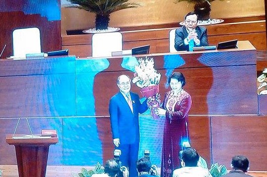 
Ông Nguyễn Sinh Hùng tặng và nhận lại bó hoa tươi thắm từ người kế nhiệm - Ảnh chụp qua màn hình
