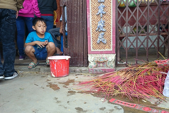 
Một đứa trẻ nhìn đống nhang cháy dở của khách hành hương để lại trước cửa chùa.
