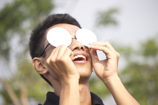 
Một thanh niên say sưa quan sát nhật thực qua kính lọc. Kính lọc giúp lọc bớt ánh sáng, tia cực tím để dễ quan sát mặt trời và bảo vệ an toàn cho mắt.
