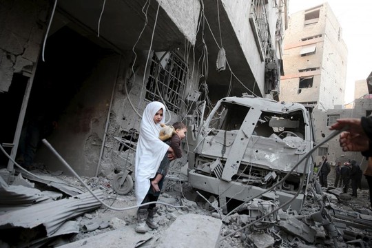 Đứa bé bồng em đứng giữa đống đổ nát không cuộc không kích ở thị trấn Douma Ảnh: REUTERS