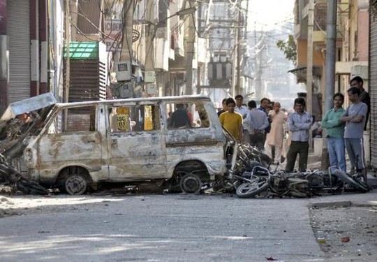Người dân đứng sau một chiếc xe bị người biểu tình đốt phá tại TP Rohtak, bang Haryana ngày 21-2. Ảnh: REUTERS