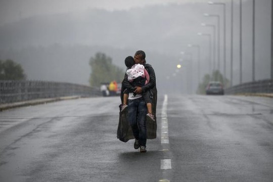 Một di dân Syria hôn con gái khi bước dưới làn mưa ở biên giới Hy Lạp và Macedonia. Ảnh: REUTERS