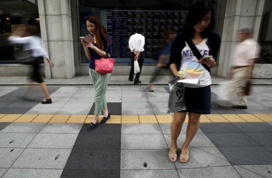 Người dân nhìn bảng điện tử chứng khoán ở Tokyo - Nhật Bản. Ảnh: REUTERS