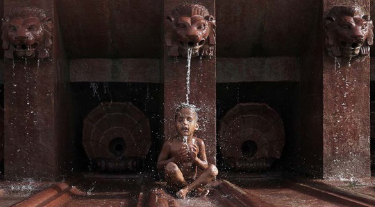 Một bé trai ngồi dưới đài phun nước ở thủ đô New Delhi - Ấn Độ Ảnh: REUTERS