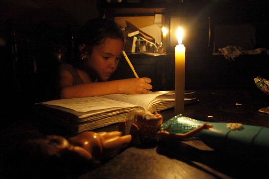 
Một bé gái làm bài tập dưới ánh nến tại nhà ở thị trấn San Cristobal - Venezuela do điện bị cắt. Ảnh: Reuters
