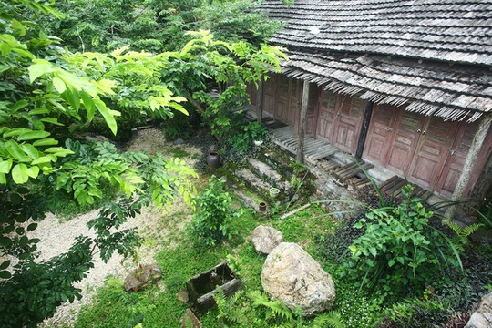Khu vườn đầy cây cỏ trước nhà gỗ kết nối với mái của ngôi nhà đá tầng dưới. Ngôi nhà tường gỗ mái ngói kiểu nông thôn Việt Nam tách hẳn với gian nhà hiện đại ở tầng bên dưới.