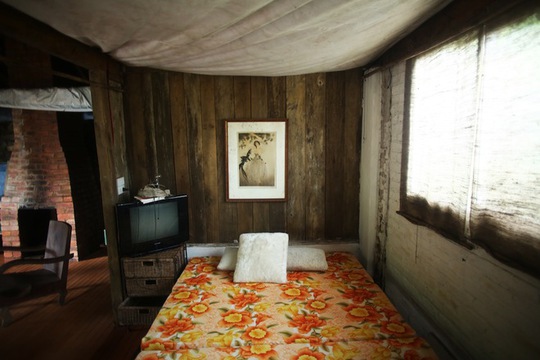 Góc phòng ngủ đơn giản trong căn nhà gỗ. Màn cửa sổ được làm từ bao tải vải thô.