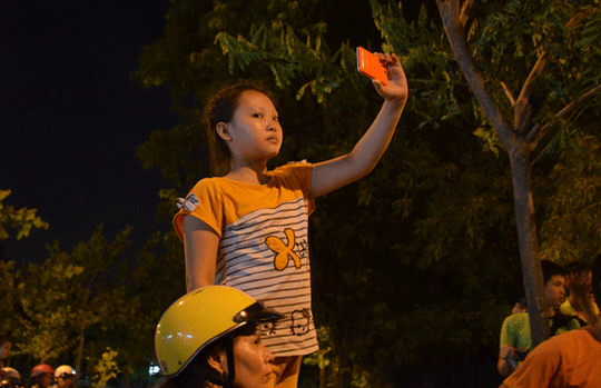 Bé gái được mẹ đỡ trên yên xe để ghi lại khoảnh khắc múa lân trong đêm trung thu