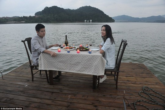 A couple enjoys their romantic meal, complete with candles and red wine, while floating in the middle of a large body of water