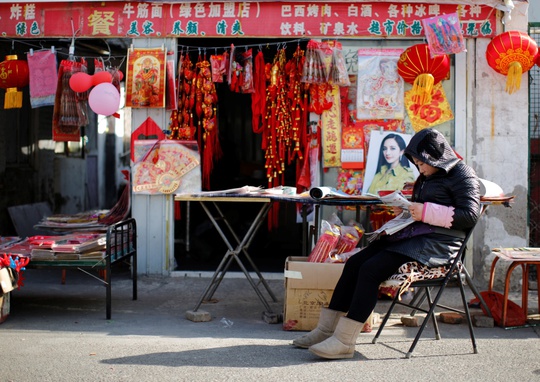 A vendor, selling traditional decorations for the upcoming Chinese Lunar New Year, reads a newspaper as she waits for customers at a migrant workers village in Beijing February 12, 2015. Photo by Kim Kyung-Hoon/REUTERS.