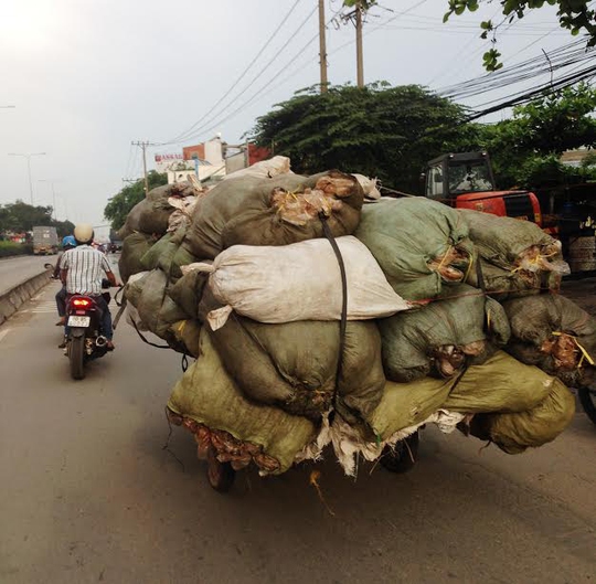 Một xe ba gác chất hàng chục bao tải ì ạch lưu thông trên Quốc lộ 1, đoạn gần chợ đầu mối nông sản thực phẩm Thủ Đức (TP HCM)Ảnh: Gia Minh