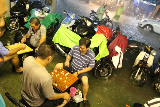 
Người dân trên đường Trần Nhân Tôn, quận 10 đánh cờ trong khi nước ngập đến chân. - Ảnh: LÊ PHONG
