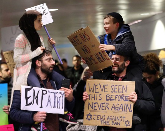 Một bé gái với khăn trùm đầu và một bé trai đội mũ Do Thái ngồi trên vai cha mình đã mỉm cười với nhau và cùng cầm những biểu ngữ. Ảnh: Chicago Tribune