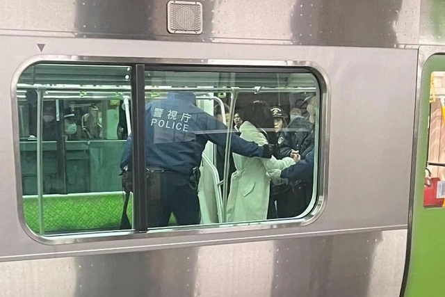 Một người mặc áo khoác trắng bị cảnh sát bao vây trong đoàn tàu đang dừng. Ảnh: NHK