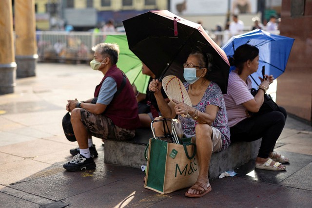 Người dân dùng dù, quạt để giải tỏa bớt nắng nóng khi ngồi bên ngoài một nhà thờ ở thủ đô Manila - Philippines ngày 26-4 Ảnh: REUTERS